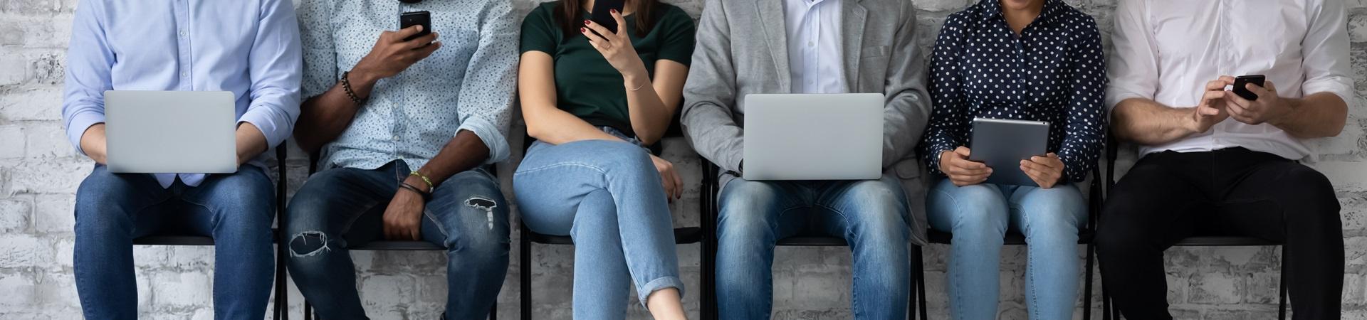 Mehrere Personen sitzen nebeneinander und nutzen Smartphones, Tablets und Laptops auf Stühlen