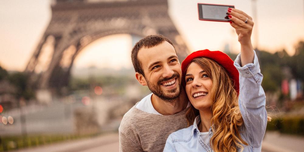 Eine Frau und ein Mann fotografieren sich mit einem Smartphone vor dem Eiffelturm in Paris