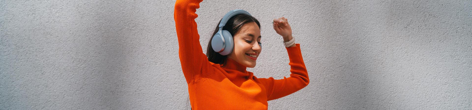 Frau mit Over-Ear-Kopfhörern tanzt vor einer Wand