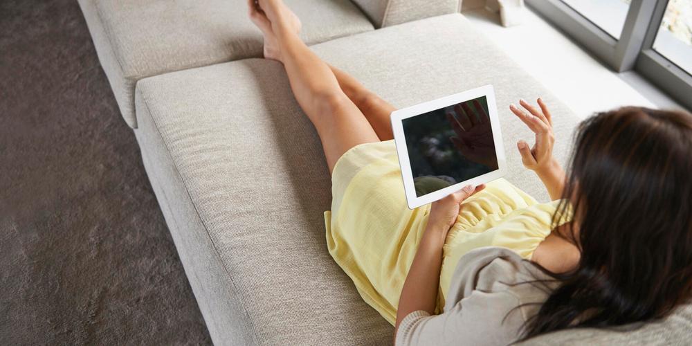 Frau liegt auf einem Sofa mit einem Tablet in der Hand