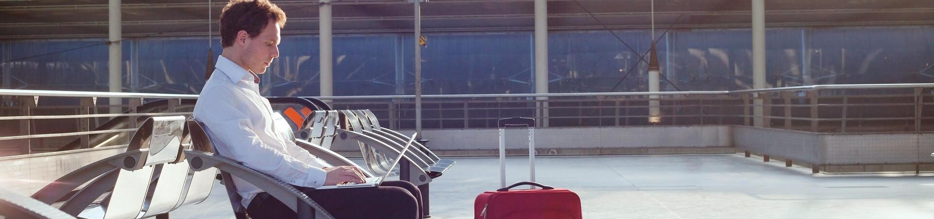 Eine Person verreist und sitzt auf einer Bank mit aufgeklapptem Laptop