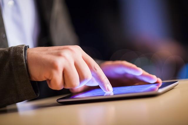 Hand bedient ein Tablet per Touchscreen auf einem Tisch in Nahaufnahme