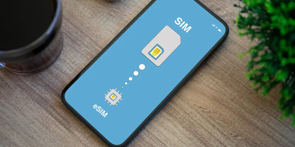 Smartphone mit Darstellung des Wechsels von physischer SIM-Karte zu eSIM auf einem Holztisch