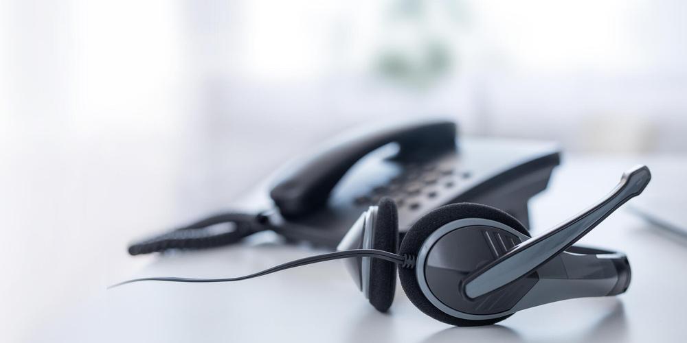 Ein an ein Kabeltelefon angebundenes Headset liegt auf einem weißen Tisch