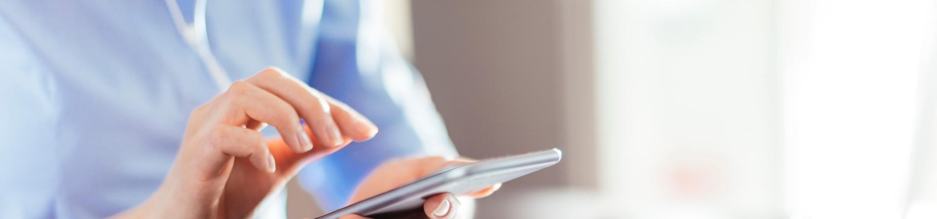 Person nutzt ein Smartphone neben einem Laptop am Schreibtisch.