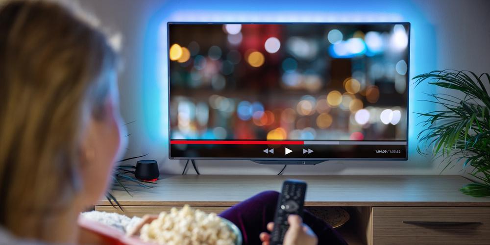 Person sitzt vor einem Fernseher und streamt einen Film 