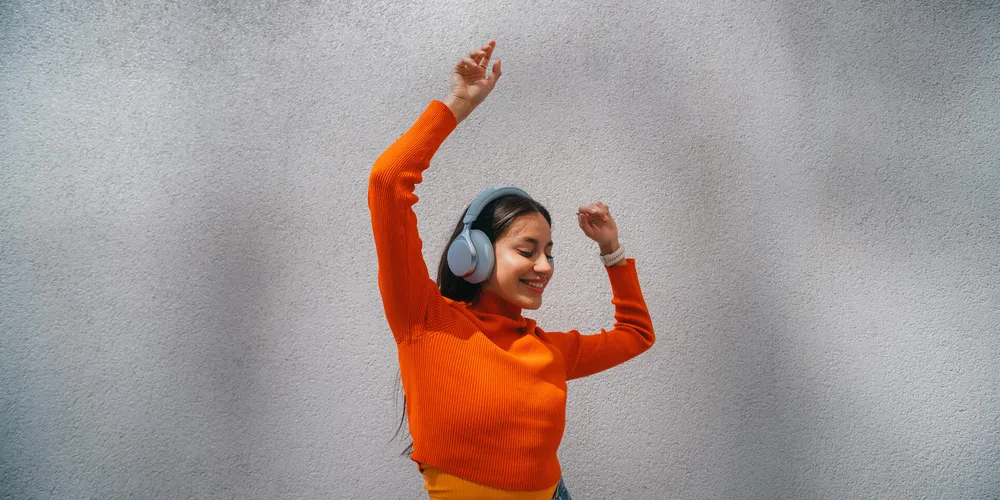 Frau mit Over-Ear-Kopfhörern tanzt vor einer Wand