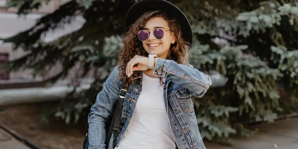 Eine lächelnde Person schaut auf die Smartwatch an ihrem Handgelenk