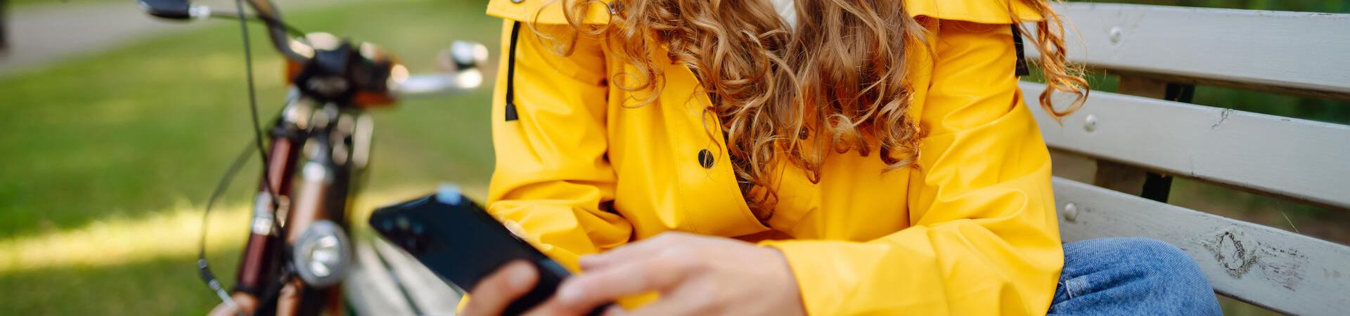 Frau mit Kopfhörern nutzt ihr Smartphone auf einer Parkbank