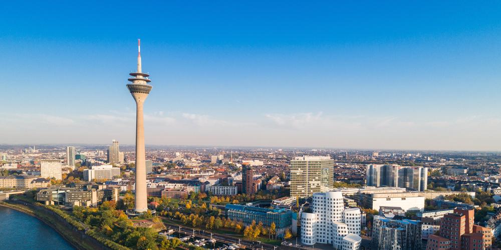 Luftaufnahme des Düsseldorfer Medienhafens mit Rheinturm und Rhein bei Tageslicht.