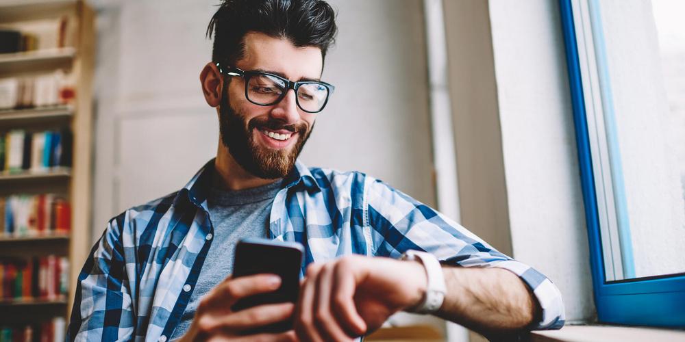 Person mit Brille schaut auf eine Smartwatch und hält ein Smartphone in der Hand