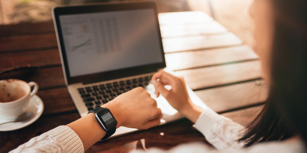 Person arbeitet am Laptop und prüft eine Nachricht auf der Smartwatch.