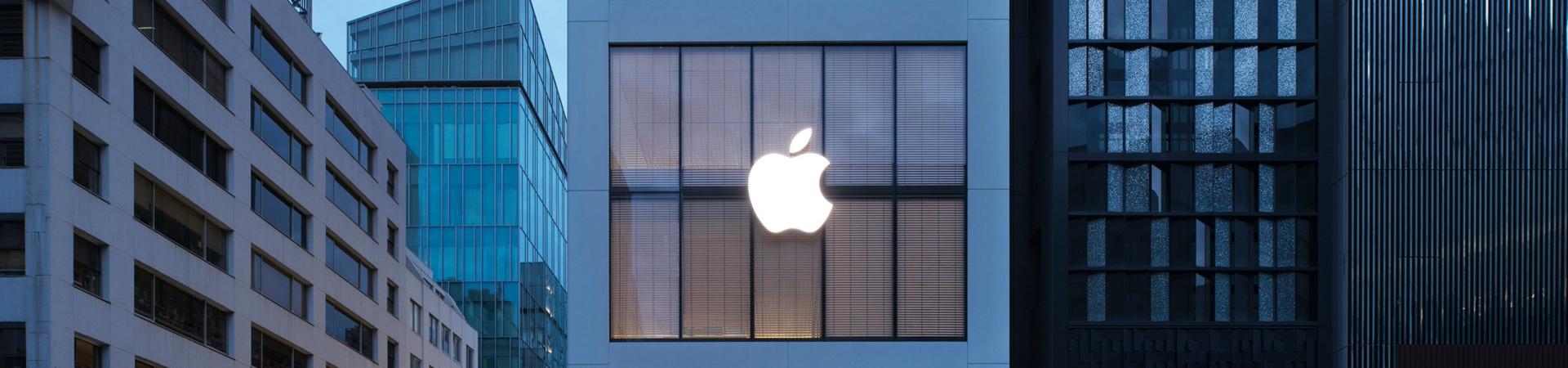Apple Store mit großem leuchtendem Apple-Logo zwischen modernen Gebäuden in einer ruhigen Straße bei Dämmerung in Tokio
