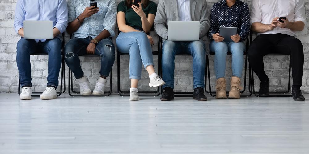 Mehrere Personen sitzen nebeneinander und nutzen Smartphones, Tablets und Laptops auf Stühlen