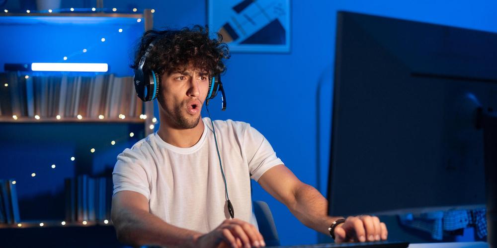 Gamer spielt zu Hause am PC mit Headset und großem Monitor
