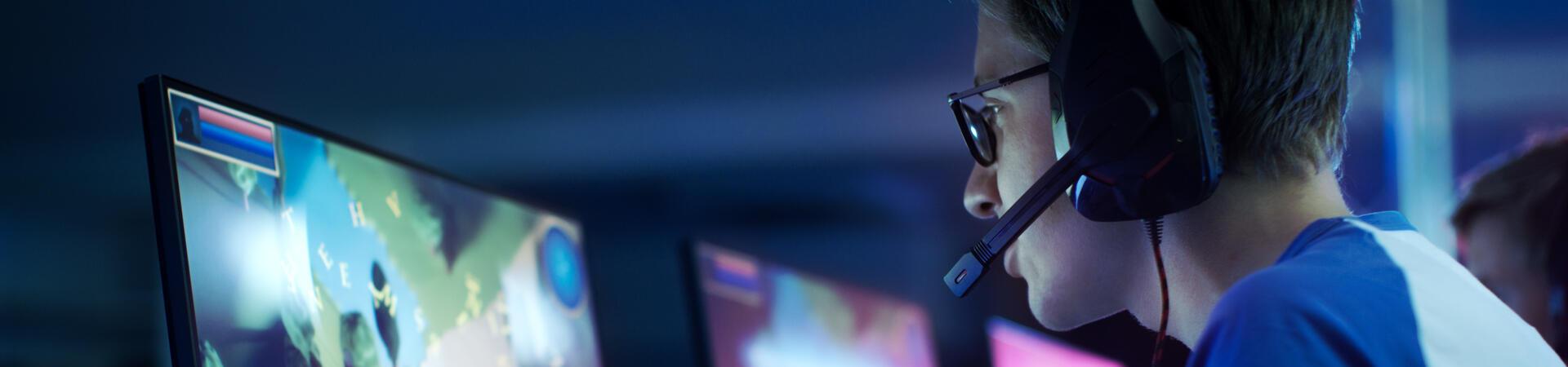Junger Gamer mit Headset spielt an mehreren Monitoren ein Online-Videospiel