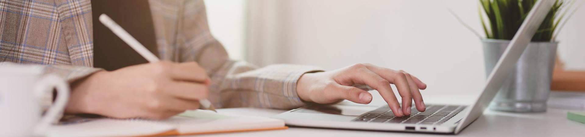 Person schreibt Notizen und arbeitet an einem MacBook am Schreibtisch.