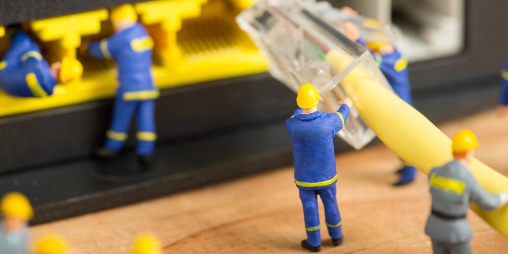 Nahaufnahme eines LAN-Kabels, das von kleinen Spielzeugbauarbeitern in Richtung eines Routers transportiert wird